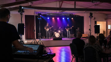 Small indoor band stage with PAR lights, moving heads, and a lighting control console