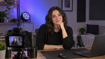 Content creator records at a desk with a black PAR light casting blue-purple color across a home studio wall
