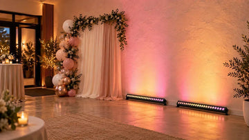 Warm white and pink wall washer lights illuminate a decorated party wall beside an indoor event entrance